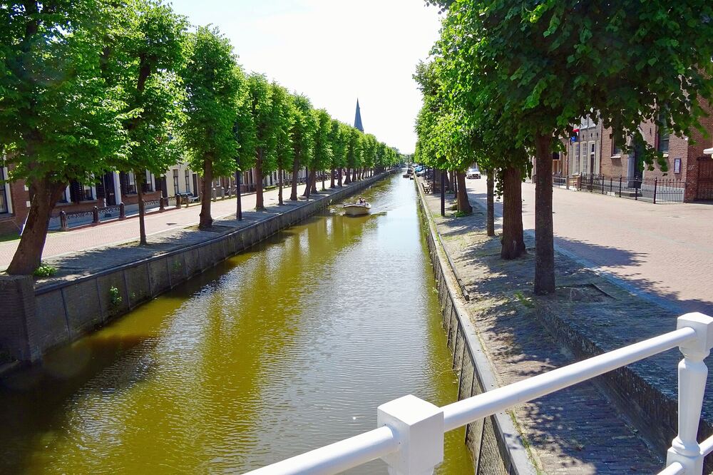De Luts in Balk tussen twee rijen lindebomen, met een bootje op het water en een kerktoren in de verte